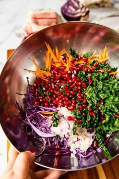 a person holding a metal bowl filled with chopped vegetables and pomegranates