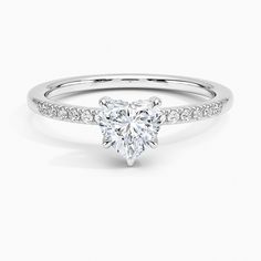 a white gold engagement ring with a heart shaped diamond in the center and pave set shoulders