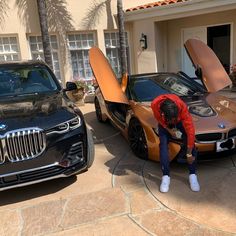 a man washing his car in front of a house with palm trees and parked cars