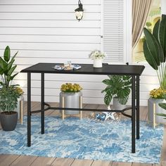 a table with potted plants on it in front of a white wall and blue rug