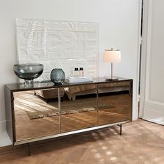 a mirrored sideboard with two vases on top and a lamp next to it