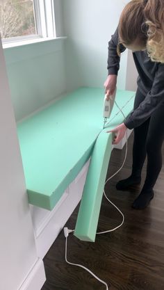 a woman using an ironing board on top of a green table in front of a window