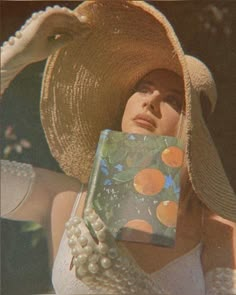 a woman wearing a large hat and holding a box with an orange design on it