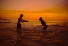 two people in the water at sunset with one holding his hand out to another person