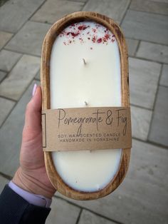 a hand holding a candle in a wooden box with a tag that says pomegranate & fig