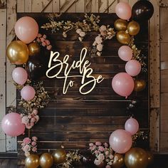 a sign that says bride to be surrounded by balloons and flowers on a wooden wall