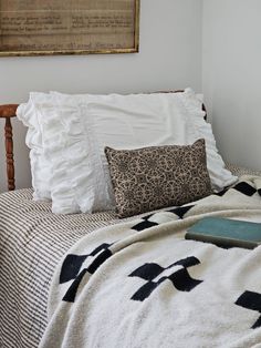 a bed with white sheets and black and white blankets on it, next to a wooden headboard