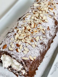 a chocolate cake with almonds and powdered sugar on top is sitting on a white platter