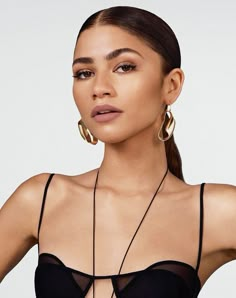 a woman wearing large gold hoop earrings and a black bra top with sheer cut fabric