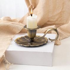 a lit candle is sitting on top of a box with a cloth draped behind it