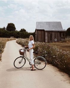 a woman standing next to a bike on a dirt road in front of a barn