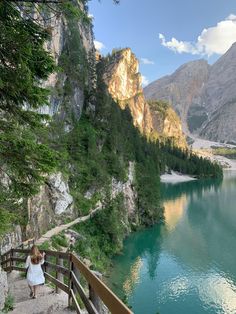 a woman standing on the side of a cliff next to a lake