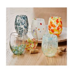 several different colored glass vases sitting on a wooden table next to wine corks