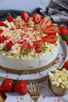 a white cake with strawberries on top and other desserts around it, along with two forks