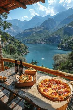 two pizzas and beer on a table with mountains in the background