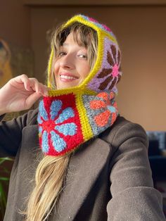 a woman wearing a knitted hat and scarf with flowers on the hood is smiling at the camera