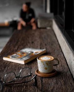 a cup of coffee sitting on top of a wooden table next to a pair of glasses