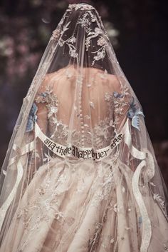 the back of a bride's wedding dress with an embroidered veil and ribbon around it