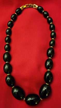 This is a beautiful Vintage beaded Necklace by D'Orlan. It has black beads that are oval shaped, with 3 different sizes and gold spacers between each bead. The back clasp is a double clasp. It is stamped DORLAN. The gold spacers and the back clasp are plated by a high standard plating process. Measured while wearing, the drop is 7.5 inches. The total open length is about 18 inches. This is such a beautiful classic necklace. This is pre-loved. As is. Traditional Black Jewelry With Oval Beads, Traditional Black Necklace With Oval Beads, Black Oval Beaded Necklaces, Elegant Black Beads With Gold Details, Traditional Black And Gold Beads, Black Necklace With Oval Spacer Beads, Black Beaded Jewelry With Oval Beads, Traditional Black Beaded Necklaces With Spacer Beads, Oval Black Beads For Jewelry Making