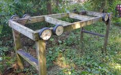 an old wooden table sitting in the middle of a forest with wheels attached to it