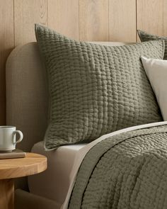 a close up of a bed with pillows and a cup on a table next to it