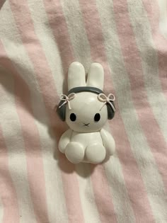 a small white rabbit with headphones on top of a pink and white striped blanket