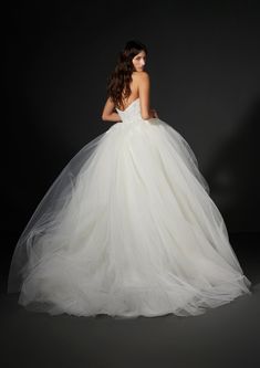 a woman in a white wedding dress standing against a black background with her back to the camera