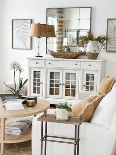 a living room filled with white furniture and lots of plants on top of a table