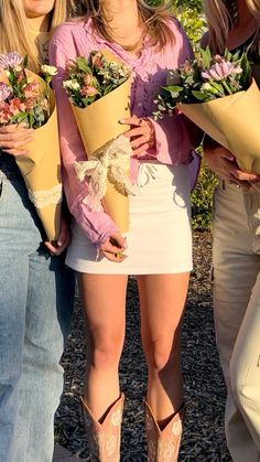 three beautiful young women standing next to each other holding flowers