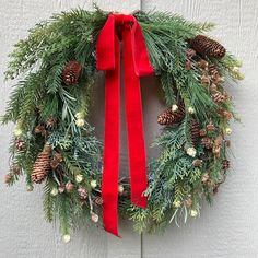 a christmas wreath with pine cones and red ribbon hanging on a white painted wooden door