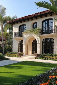 a large white house with lots of windows and plants on the front lawn, surrounded by palm trees