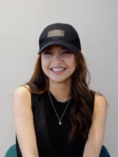 a woman with long hair wearing a black hat and smiling at the camera while sitting on a chair