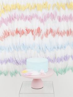 a cake sitting on top of a pink plate next to a wall with colorful feathers