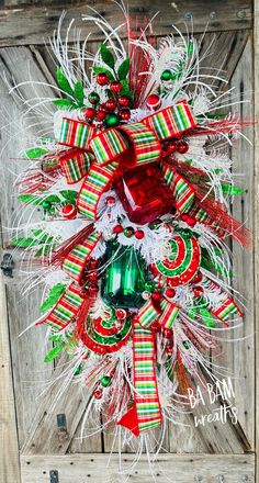 a christmas wreath with red, green and white ribbons hanging on a wooden door frame