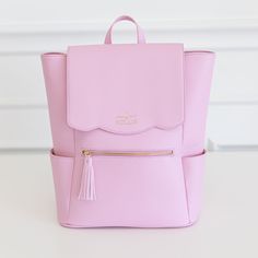 a pink backpack sitting on top of a white table with a tasseled handle