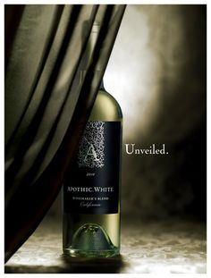 a bottle of white wine sitting on top of a table next to a black curtain