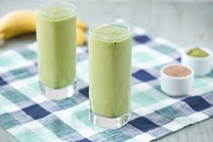 two glasses filled with green smoothie sitting on top of a checkered table cloth