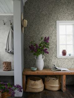 a vase with purple flowers sitting on top of a wooden bench next to a window