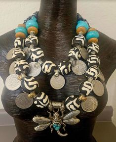 Hello Gorgeous! This big, bold and chunky Zebu* batik bone and Kuchi coin Statement Necklace is for jewelry addicts only! This OOAK piece contains the following components: bone, silver tone metal spacers, vintage Kuchi coins, turquoise-green colored Magnesite rondelles, juniper wood rondelles, Yoruba brass rings, aluminum-wood beads and faceted crystals. This is versatile in that you can flatten the coins on the interior strand or layer them on top of the outer strand (see photographs). Adjusts from 23-26". The Tibetan Repousse Dragonfly Pendant measures 3.25" x 3.5" and features an inlaid turquoise cabochon. Closes with a silver tone lobster claw clasp and a 3" extender chain with Kuchi coin dangle. Totally Haute Couture! *The bone used in this piece is from African domesticated cattle k Afrocentric Jewelry Handmade, Luxury Large Bead Amulet Jewelry, Rocker Chic Accessories, African Jungle, Juniper Wood, Artisan Jewelry Necklaces, Brass Rings, Unique Pendant Necklace, Tibetan Jewelry