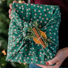 a person holding a wrapped present in front of a christmas tree with orange slices and rosemary