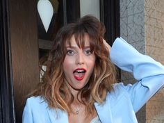 a woman with her hand on her head standing in front of a door and looking at the camera