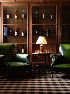 a living room with two green chairs and a table in front of a bookcase