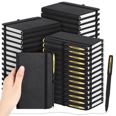 a hand is holding a notebook and pen in front of several stacks of black binders