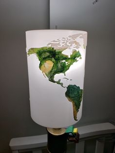 a white lamp with a green world map on it's side and the light is turned on