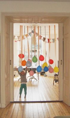 a little boy standing in front of an open door with balloons hanging from the ceiling