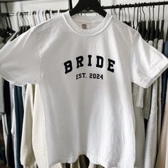 a white t - shirt with the word bride on it hanging in front of clothes