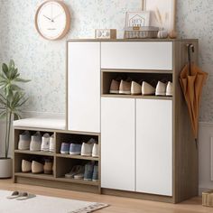 a white cabinet with shoes on it in front of a wall clock and potted plant