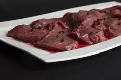 a white plate topped with meat on top of a black table next to a knife and fork