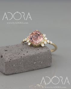 a pink diamond ring sitting on top of a rock with white diamonds around the band