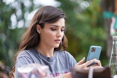 a woman sitting at an outdoor table looking at her cell phone while holding a water bottle